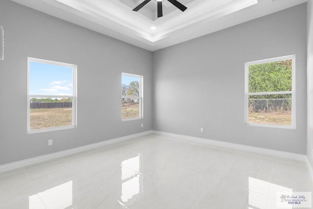 empty room with a tray ceiling, baseboards, a ceiling fan, and plenty of natural light