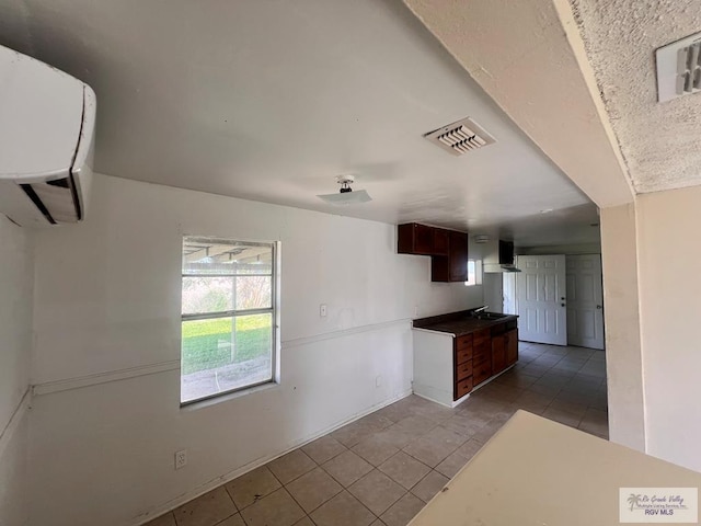 kitchen with light tile patterned floors, wall chimney exhaust hood, sink, and a wall unit AC