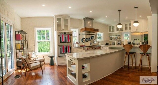 kitchen with dark hardwood / wood-style flooring, premium range hood, stainless steel appliances, white cabinets, and hanging light fixtures