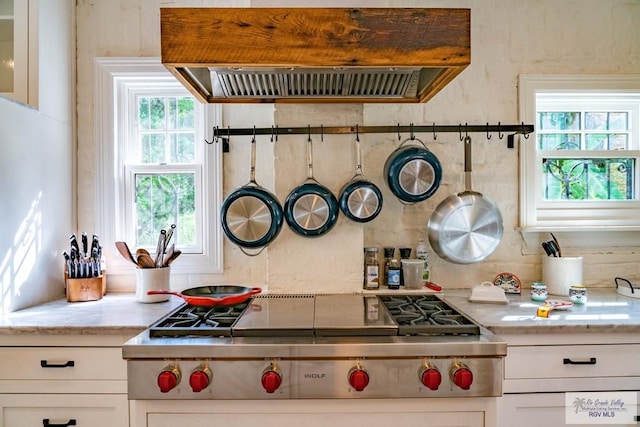 kitchen with stainless steel gas stovetop, a wealth of natural light, white cabinetry, and range hood