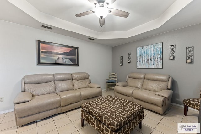 living room featuring a raised ceiling, ceiling fan, and light tile patterned flooring