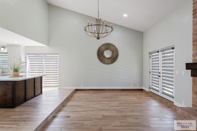 unfurnished dining area featuring light wood finished floors, baseboards, high vaulted ceiling, and an inviting chandelier