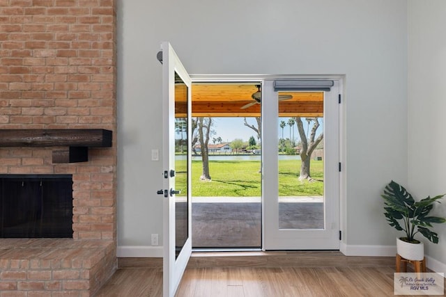 doorway to outside featuring a brick fireplace, ceiling fan, baseboards, and wood finished floors