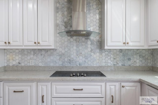 kitchen featuring tasteful backsplash, white cabinets, wall chimney exhaust hood, light stone counters, and black electric stovetop