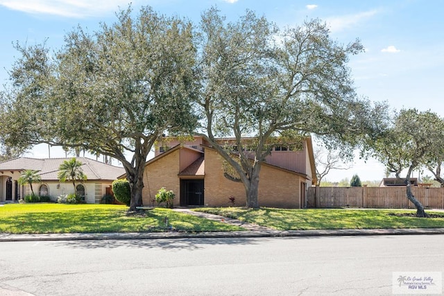 mid-century inspired home featuring driveway, brick siding, a front yard, and fence