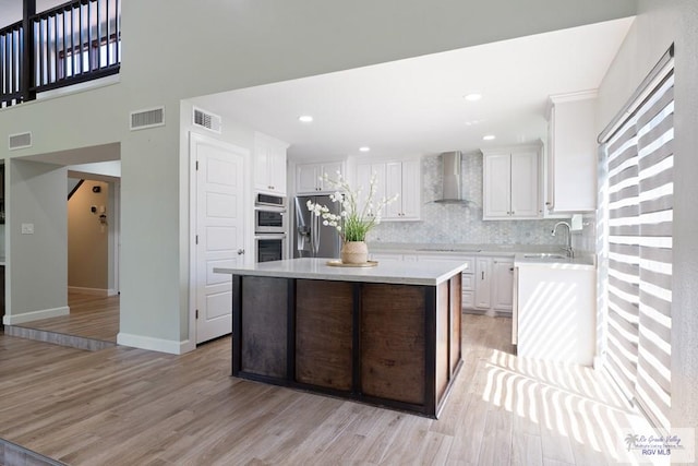 kitchen featuring white cabinets, light countertops, appliances with stainless steel finishes, a center island, and wall chimney exhaust hood