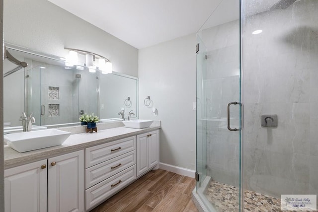 bathroom featuring double vanity, wood finished floors, a sink, and a shower stall