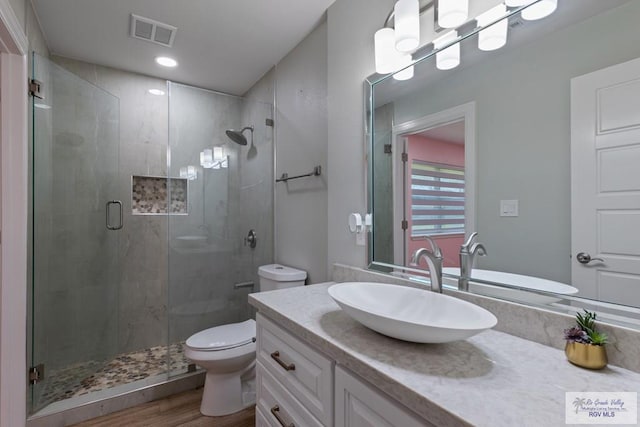 bathroom with a stall shower, visible vents, toilet, wood finished floors, and vanity