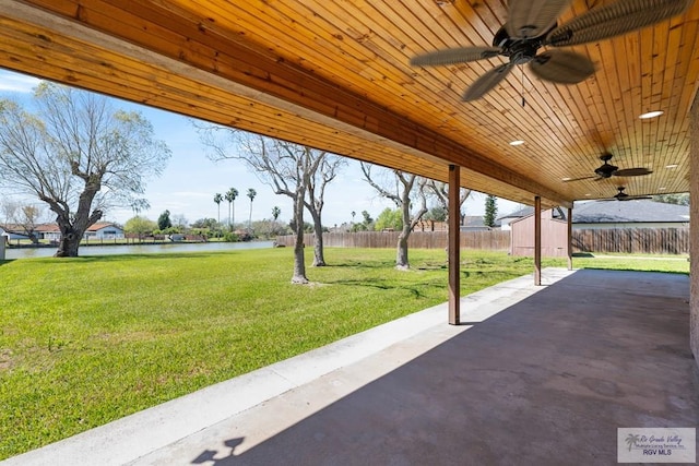 view of patio / terrace featuring ceiling fan, a water view, fence, and an outbuilding