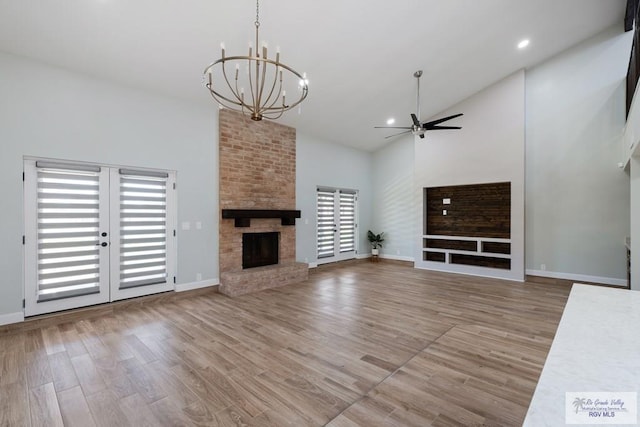 unfurnished living room featuring high vaulted ceiling, ceiling fan with notable chandelier, a brick fireplace, and wood finished floors