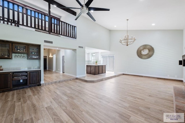 unfurnished living room featuring visible vents, light wood-style flooring, baseboards, and ceiling fan with notable chandelier