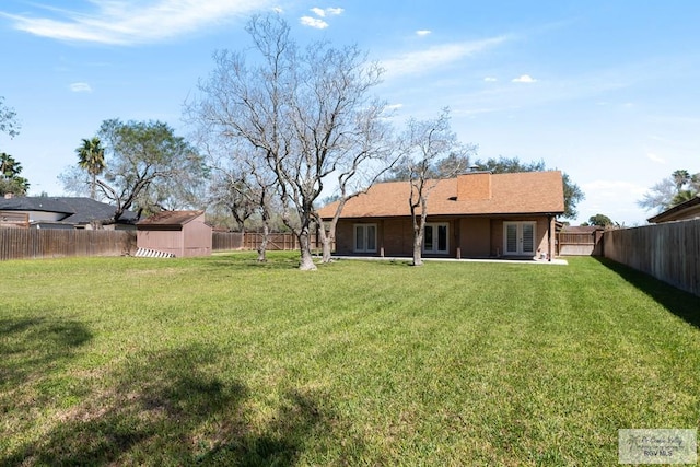 rear view of house featuring a lawn, a fenced backyard, a storage unit, an outdoor structure, and a patio area