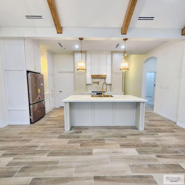 kitchen with white cabinets, stainless steel refrigerator, pendant lighting, a spacious island, and beam ceiling