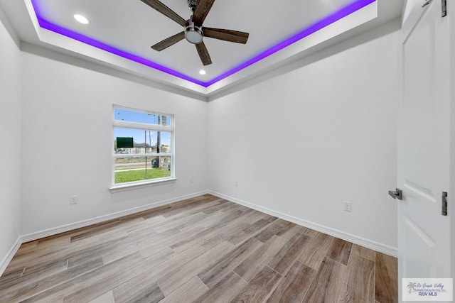 unfurnished room featuring ceiling fan, light wood-type flooring, and a tray ceiling