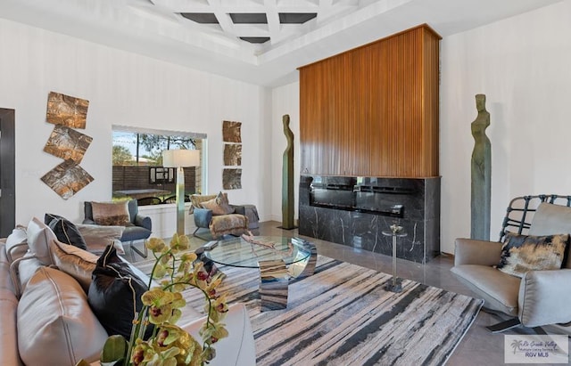 living room with a tile fireplace, coffered ceiling, ceiling fan, a towering ceiling, and a tray ceiling