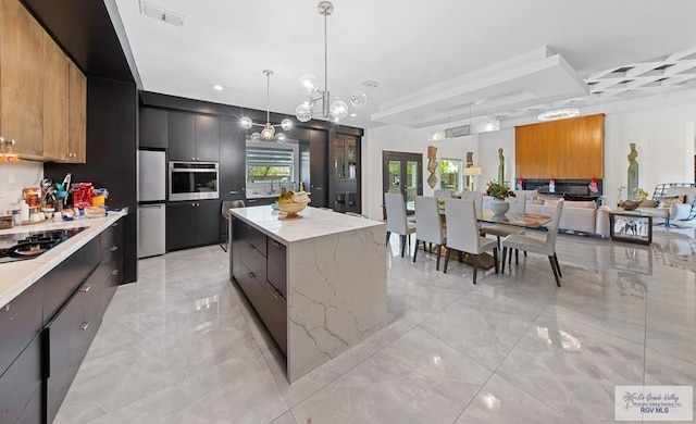 kitchen with hanging light fixtures, appliances with stainless steel finishes, a notable chandelier, a kitchen island, and light stone counters