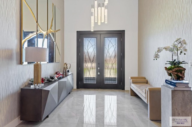 foyer featuring a chandelier, a healthy amount of sunlight, a towering ceiling, and french doors