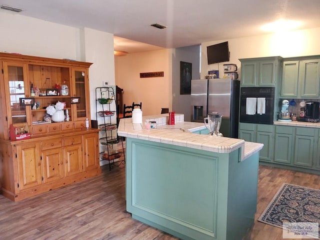 kitchen with stainless steel fridge with ice dispenser, tile counters, oven, and hardwood / wood-style floors