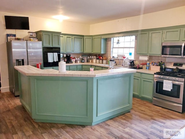 kitchen with appliances with stainless steel finishes, light hardwood / wood-style floors, tile counters, and green cabinetry