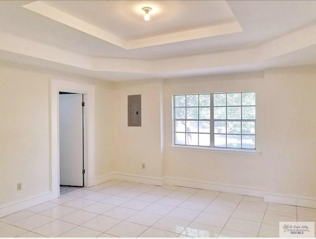 tiled spare room featuring electric panel and a tray ceiling