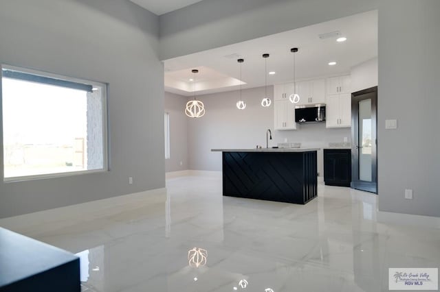 kitchen with stainless steel microwave, pendant lighting, a tray ceiling, white cabinets, and marble finish floor