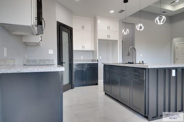 kitchen with visible vents, an island with sink, a sink, white cabinetry, and marble finish floor