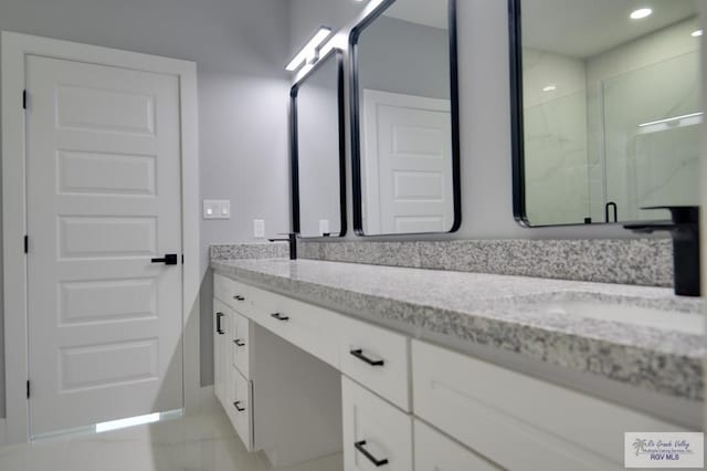 full bathroom with a marble finish shower, double vanity, and a sink