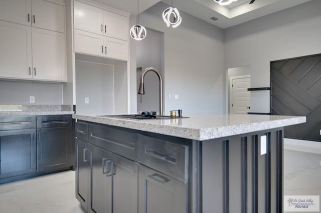 kitchen with visible vents, a sink, light stone counters, a kitchen island, and white cabinetry