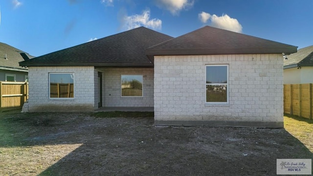 back of property with fence and a shingled roof