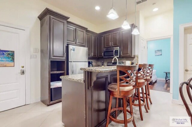 kitchen featuring a kitchen bar, dark brown cabinets, stainless steel appliances, and light stone counters