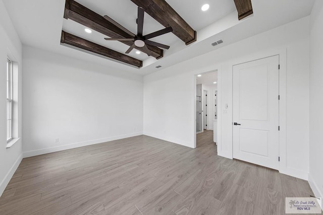 spare room with ceiling fan, beam ceiling, a raised ceiling, and light hardwood / wood-style flooring