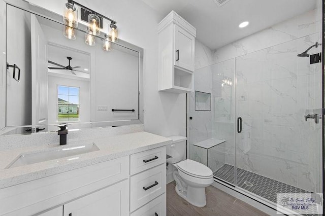 bathroom featuring ceiling fan, vanity, a shower with door, and toilet