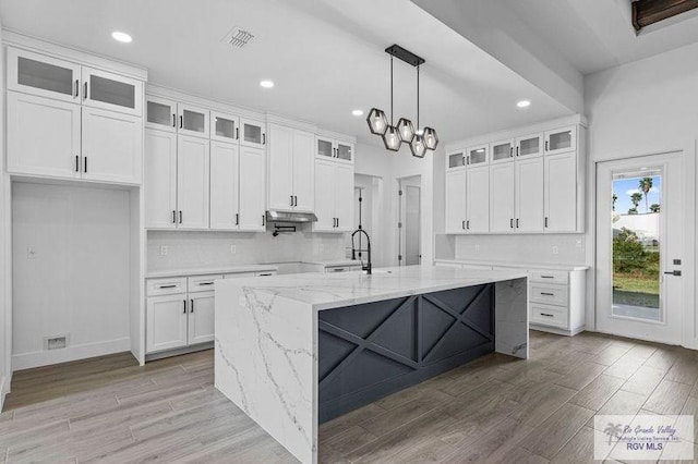 kitchen featuring sink, an island with sink, light stone counters, and white cabinetry