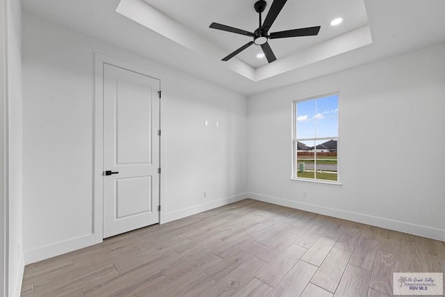 empty room with ceiling fan and a tray ceiling