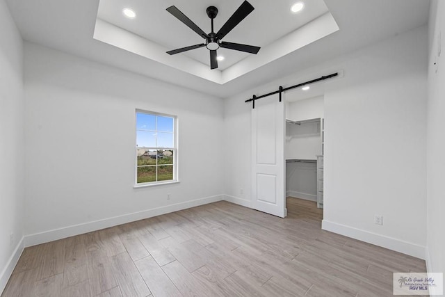 unfurnished bedroom featuring ceiling fan, a tray ceiling, a walk in closet, and a barn door