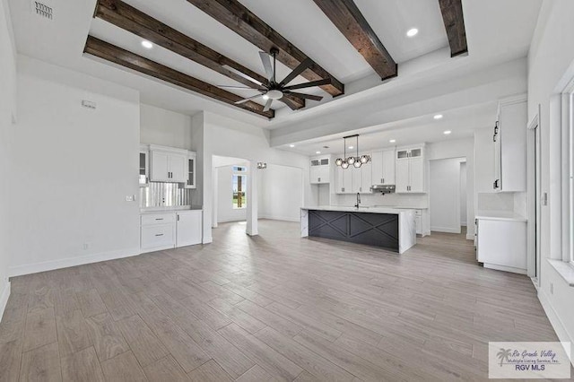 unfurnished living room with ceiling fan, light hardwood / wood-style floors, a raised ceiling, and beam ceiling