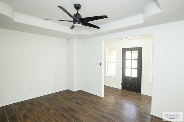 empty room with a raised ceiling, ceiling fan, and dark hardwood / wood-style flooring