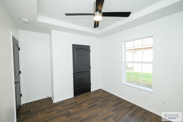 unfurnished room featuring dark hardwood / wood-style floors, ceiling fan, and a raised ceiling