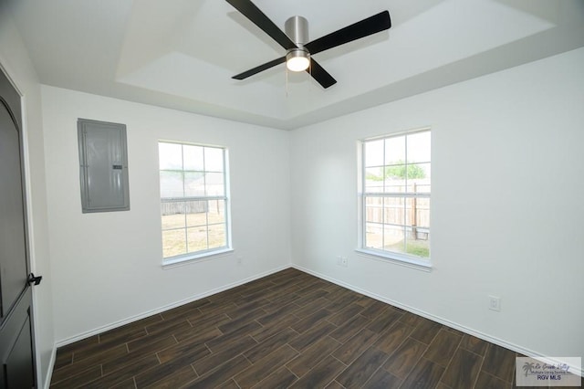 unfurnished room with a tray ceiling, electric panel, ceiling fan, and dark hardwood / wood-style floors