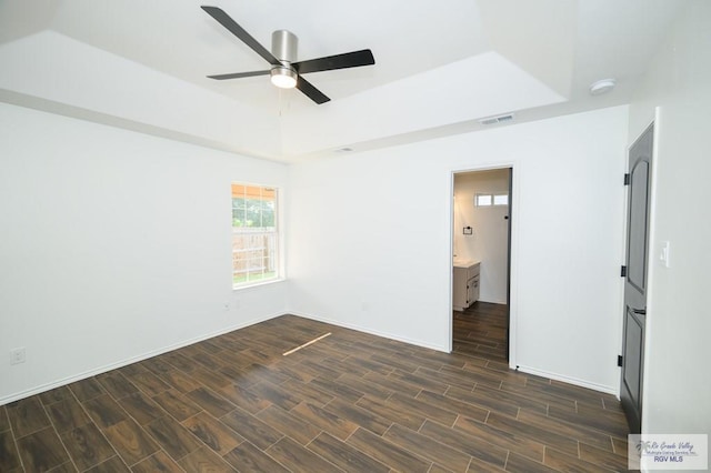 spare room with dark hardwood / wood-style floors, ceiling fan, and a raised ceiling