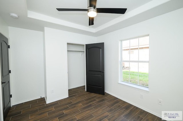 unfurnished bedroom featuring dark hardwood / wood-style flooring, a closet, ceiling fan, and a tray ceiling