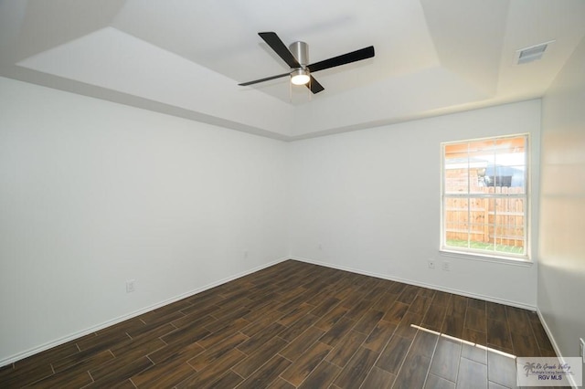 spare room featuring a raised ceiling, ceiling fan, and dark wood-type flooring