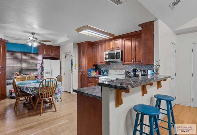 kitchen with visible vents, backsplash, light wood-style flooring, a peninsula, and white appliances