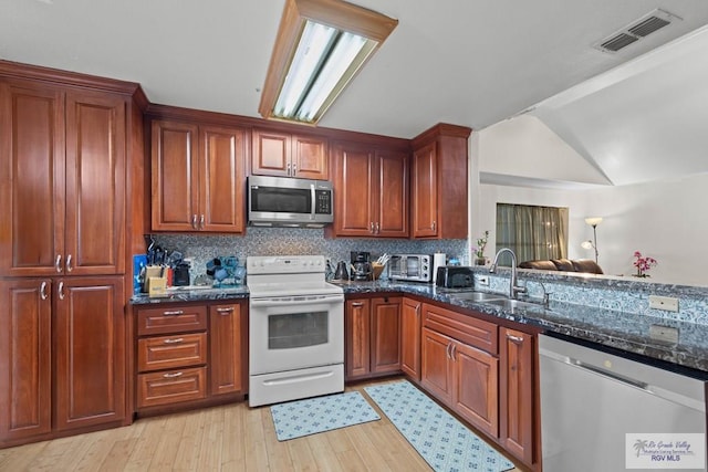 kitchen featuring visible vents, a sink, dark stone countertops, appliances with stainless steel finishes, and light wood finished floors