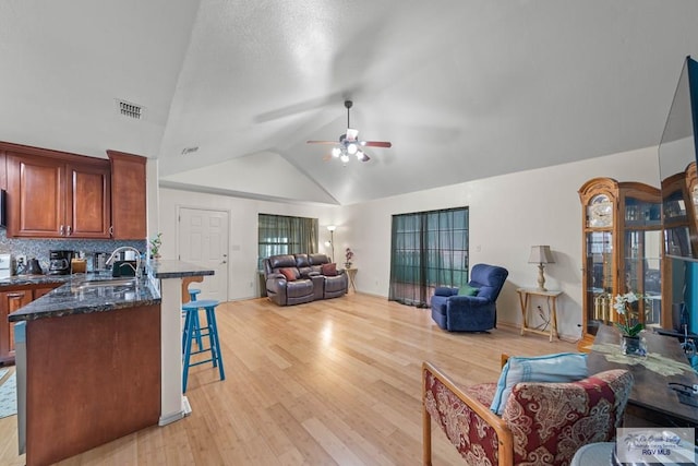 living area featuring visible vents, lofted ceiling, light wood-style flooring, and a ceiling fan