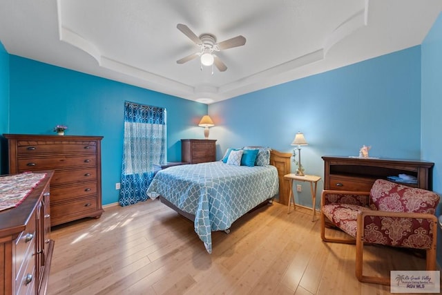 bedroom with baseboards, a raised ceiling, a ceiling fan, and light wood finished floors