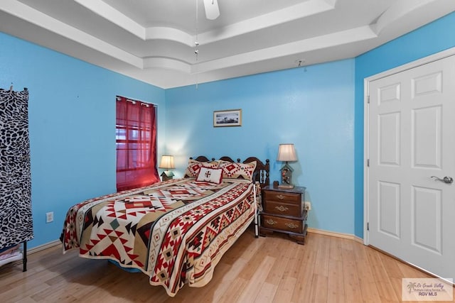 bedroom featuring ceiling fan, baseboards, a tray ceiling, and wood finished floors