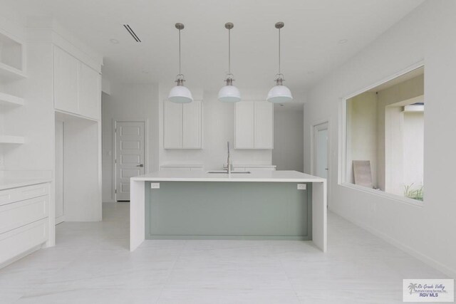 kitchen featuring white cabinets, sink, decorative light fixtures, and an island with sink