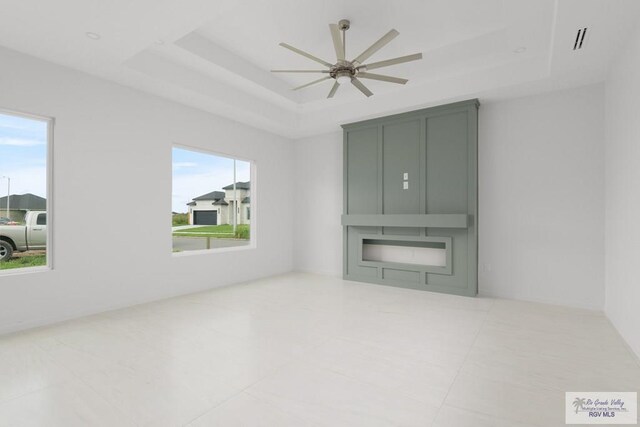 unfurnished room featuring a raised ceiling, ceiling fan, and plenty of natural light