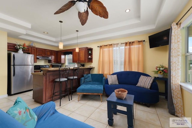 tiled living room featuring ceiling fan and a raised ceiling